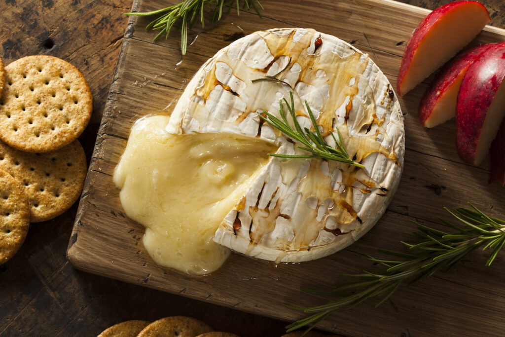 Baked Brie cheese on the wooden chopping board with apple and cookies