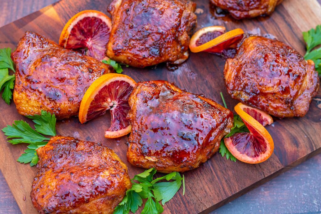 Smoked chicken thighs on wooden plate with slices of orange