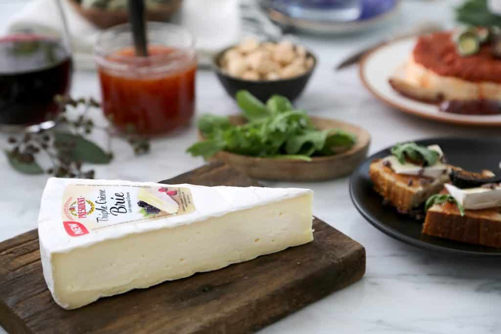 Slice of Brie cheese on the wooden chopping board with food
